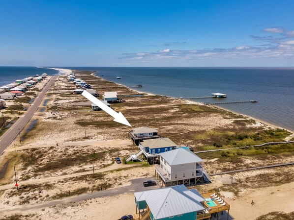 Vista aérea de una zona costera con propiedades frente al mar, una carretera y un muelle que se adentra en el agua.