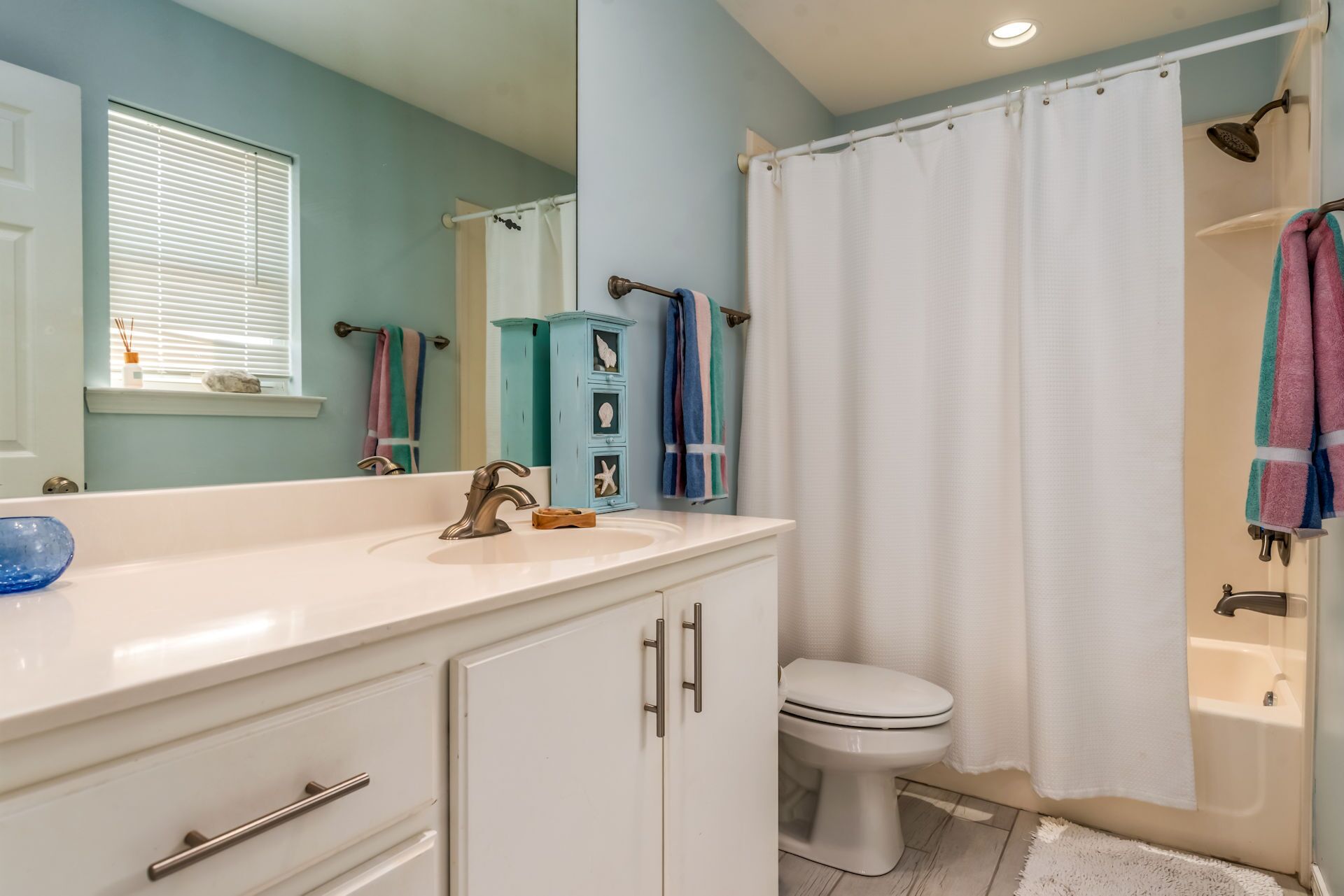 A bathroom with a white sink, a toilet, and a shower curtain. There are towels hanging on a rack and a cabinet with drawers.
