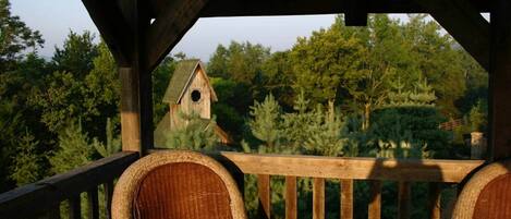 A wooden deck with wicker chairs and a view of a birdhouse in a forested area.