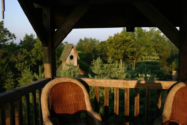 A wooden deck with wicker chairs and a view of a birdhouse in a forested area.