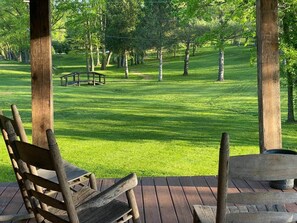 Een houten terras met een bankje, met uitzicht op een verzorgd gazon met bomen.