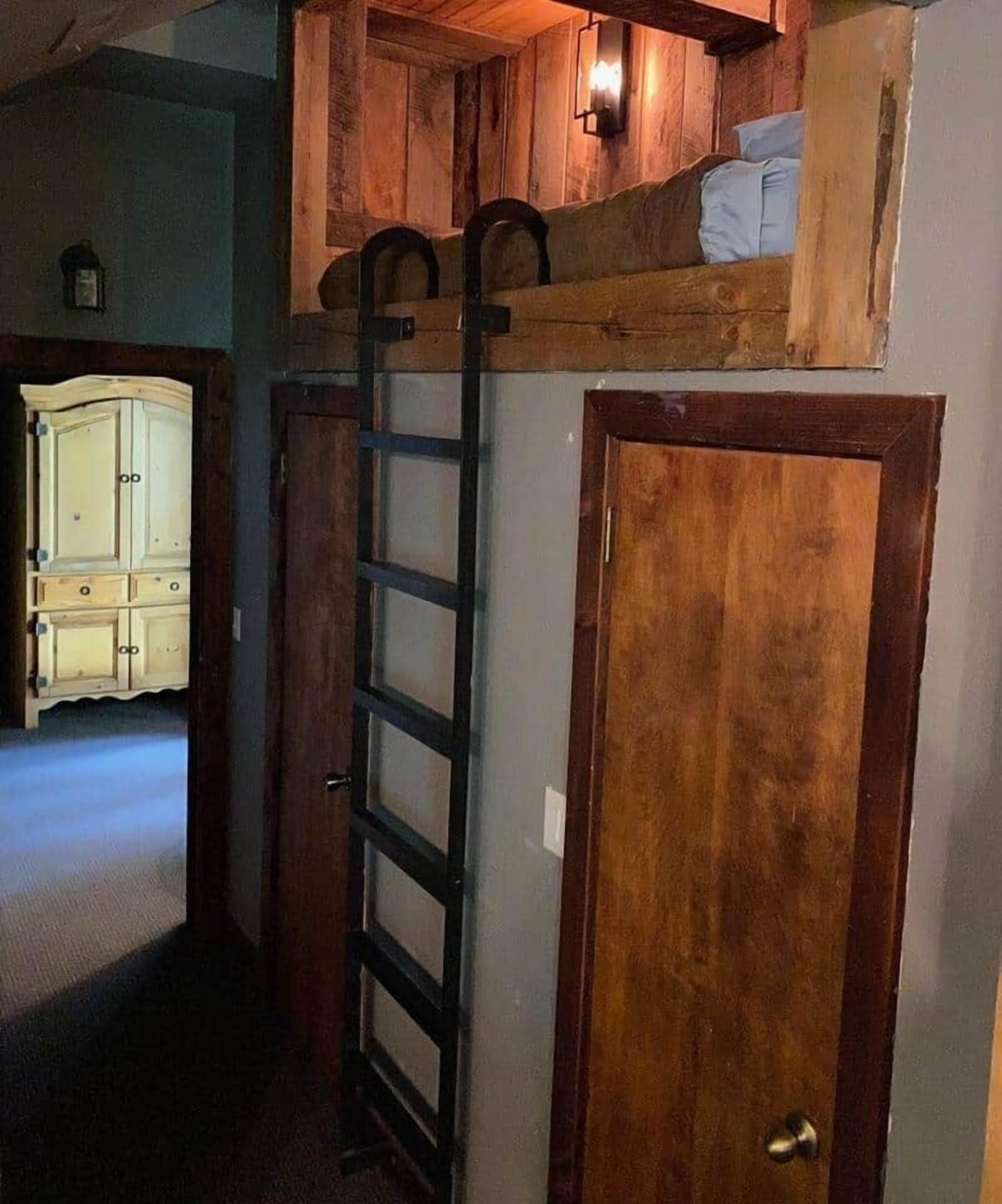 Una habitación con una cama alta, una escalera y una puerta de madera.