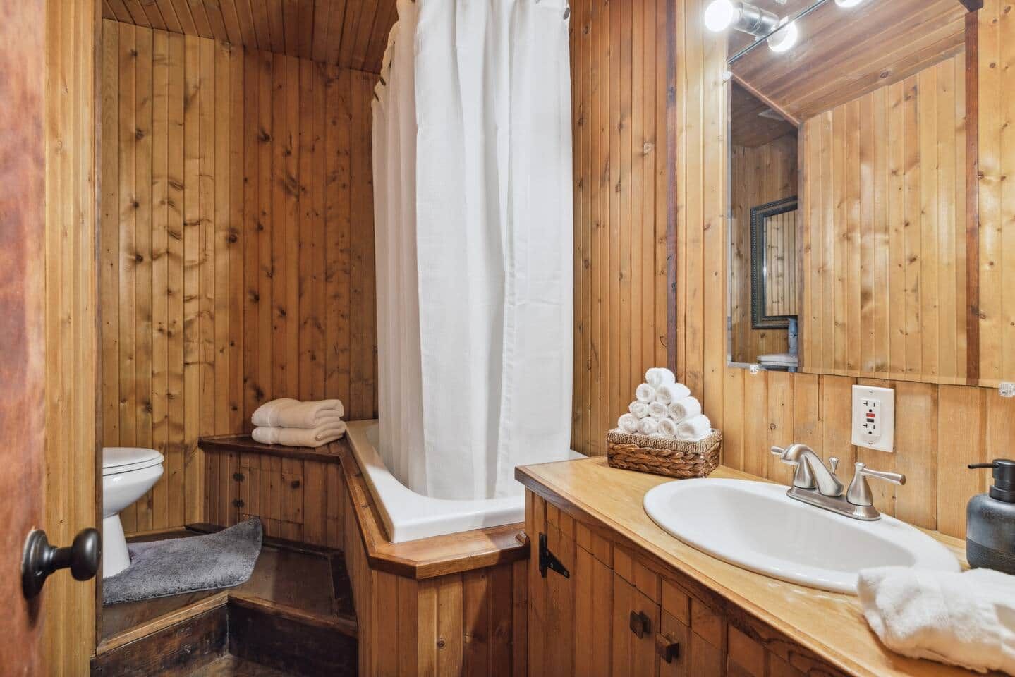 A wooden bathroom with a bathtub, a toilet, a sink, and a mirror.