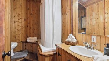 A wooden bathroom with a bathtub, a toilet, a sink, and a mirror.