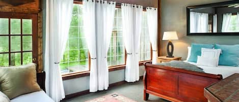 Una habitación con cama de madera, una mesita de noche, un espejo y una ventana con cortinas blancas.