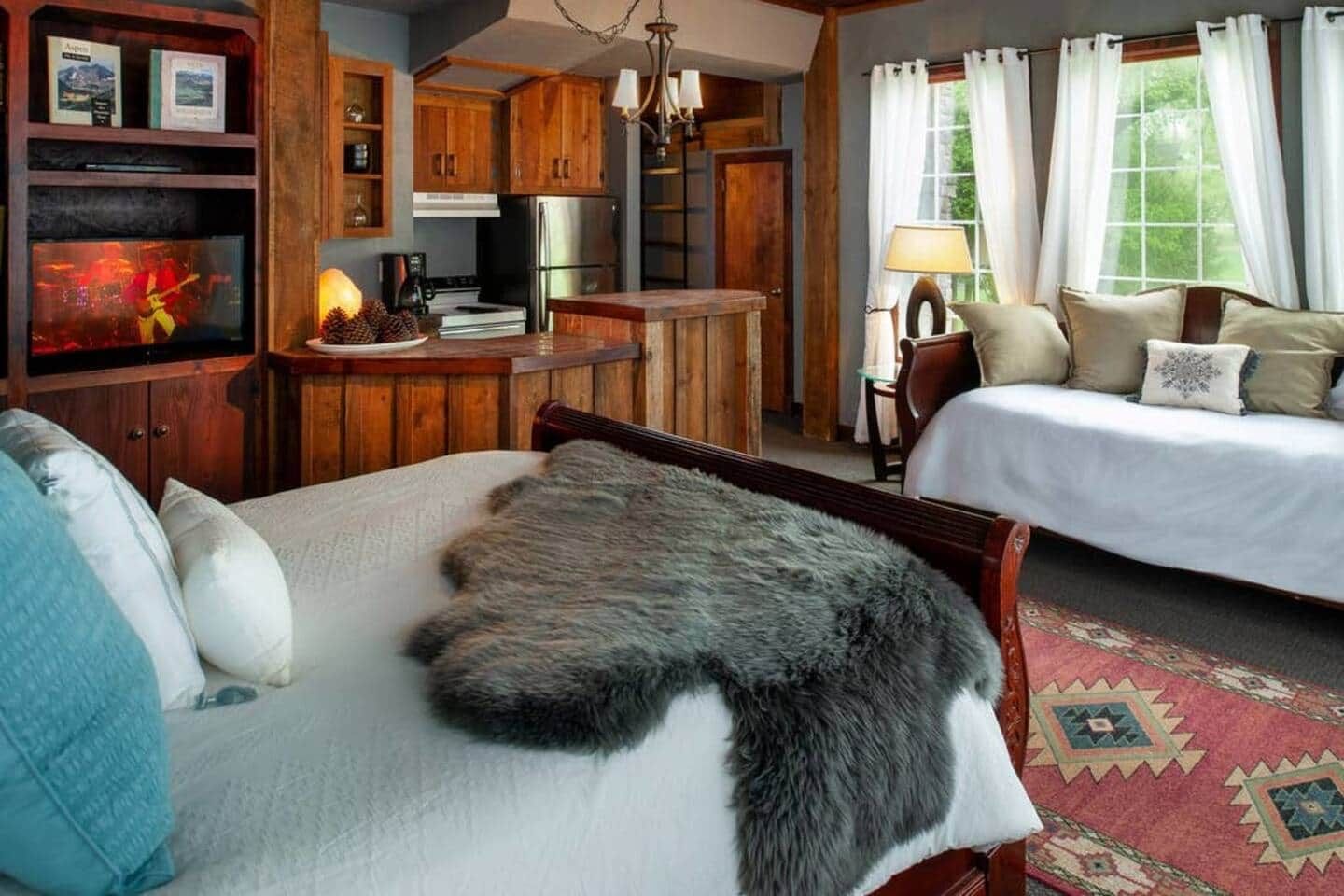 A cozy room with a bed, a sofa, a fireplace, and a kitchen area.