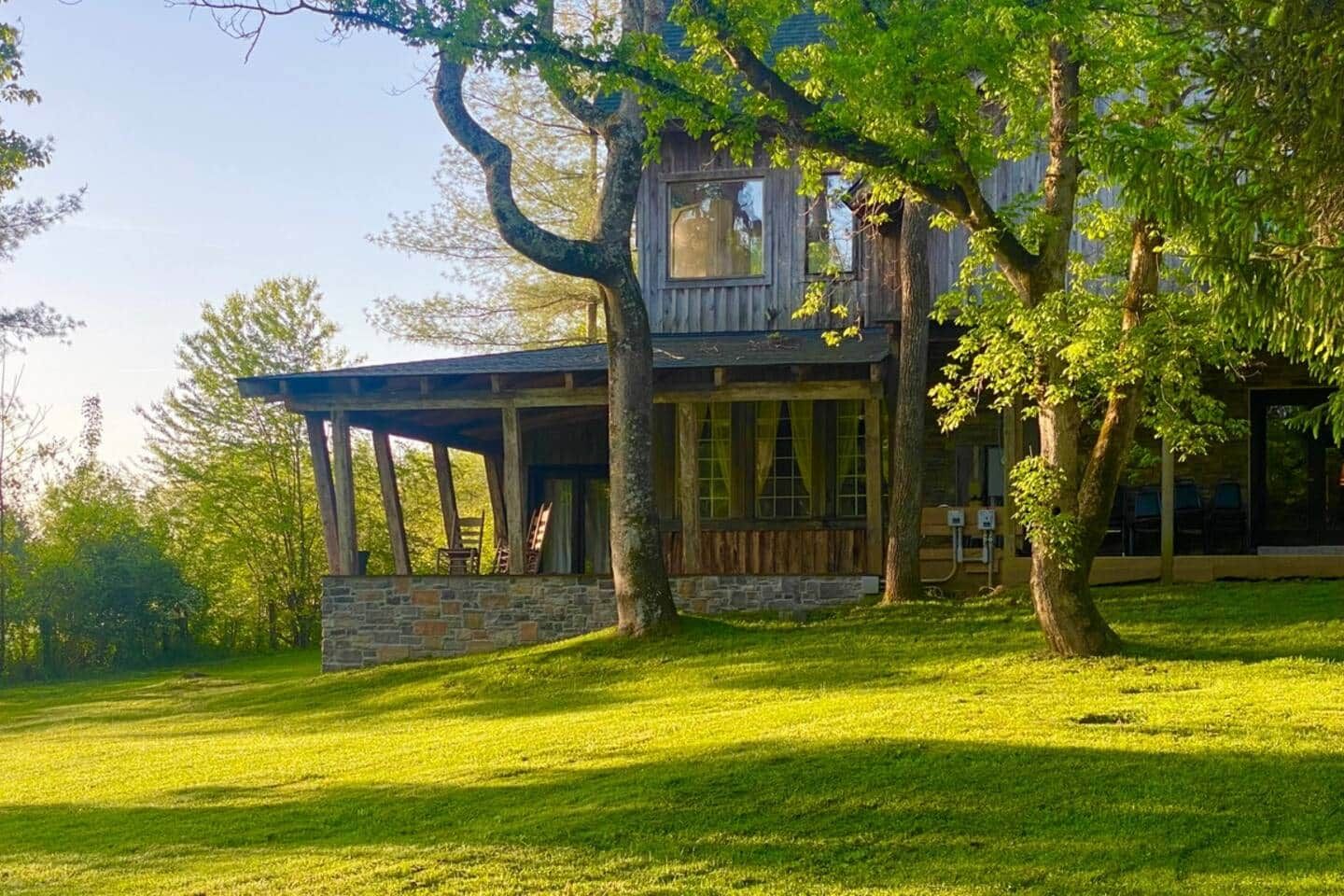 A rustic cabin with a stone foundation, wooden walls, and a covered porch with chairs.