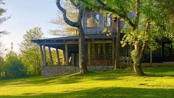 A rustic cabin with a stone foundation, wooden walls, and a covered porch with chairs.