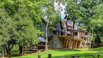 Une cabane en bois rustique, posée sur des fondations en pierre, entourée d’une végétation luxuriante et agrémentée d’une table de pique-nique.