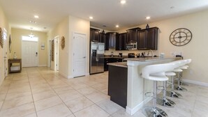 Una cocina amplia con armarios oscuros, una isla central con taburetes de bar y un reloj grande en la pared.