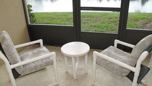 A room with two white chairs and a small table, a large window with a view of a lake and greenery. - 3 Bedroom Oakwater Resort Nearst Disney 3owt27ow33 (St. Cloud)