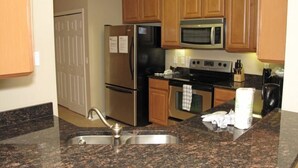 A kitchen with wooden cabinets, a stainless steel refrigerator, a microwave, and granite countertops. - 3 Bedroom Oakwater Resort Nearst Disney 3owt27ow33 (St. Cloud)