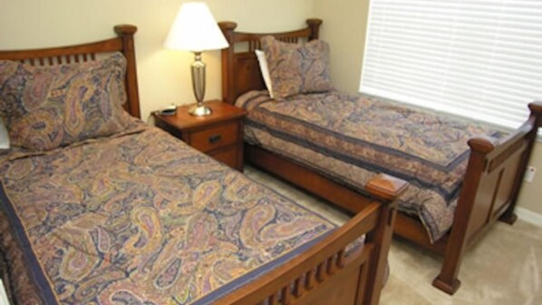 A bedroom with two wooden beds, each with a patterned bedspread, a bedside table with a lamp, and a window with blinds. - Oakwater Resort, Amazing Location (St. Cloud)