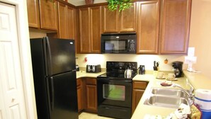 A kitchen with wooden cabinets, a black refrigerator, a microwave, an oven, and a sink.