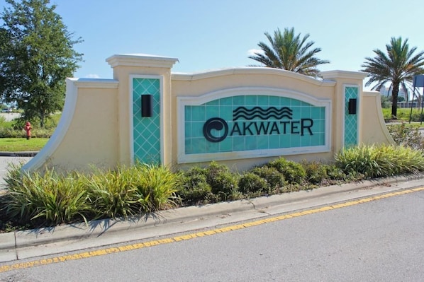 A sign with the name "AKWATER" and a wave symbol, surrounded by greenery and a curved wall.