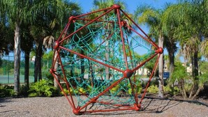 A geometric structure with a network of ropes and poles, surrounded by palm trees and a gravel ground. - Oakwaterresort Near Disney h (St. Cloud)