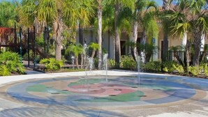 A circular water feature with a fountain in the center, surrounded by palm trees and a building with a tiled roof. - Oakwaterresort Near Disney h (St. Cloud)