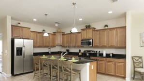 Una cocina con gabinetes de madera, un refrigerador de acero inoxidable, un microondas y una isla central con taburetes de bar.