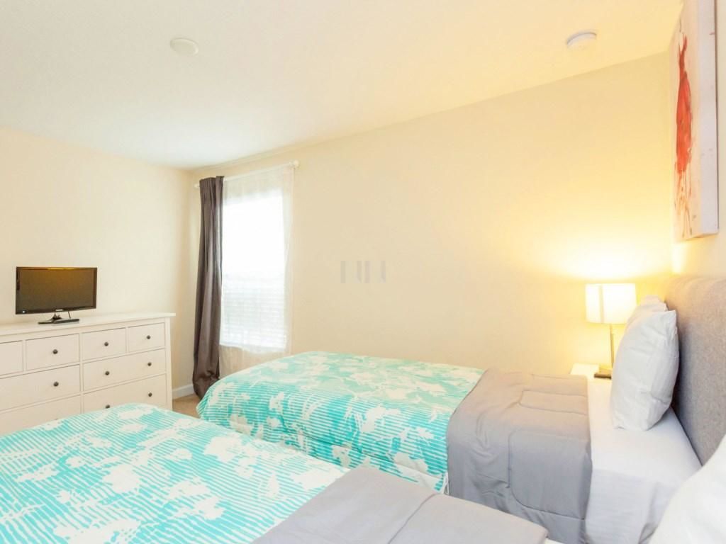 A hotel room with two beds, a TV on a dresser, a window with curtains, and a wall-mounted lamp.