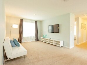 A modern living room with a white sofa, a flat-screen TV mounted on the wall, and a white entertainment unit with storage.