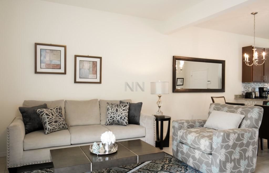 Una sala de estar con sofá, sillón, mesa de centro y un comedor con candelabro.
