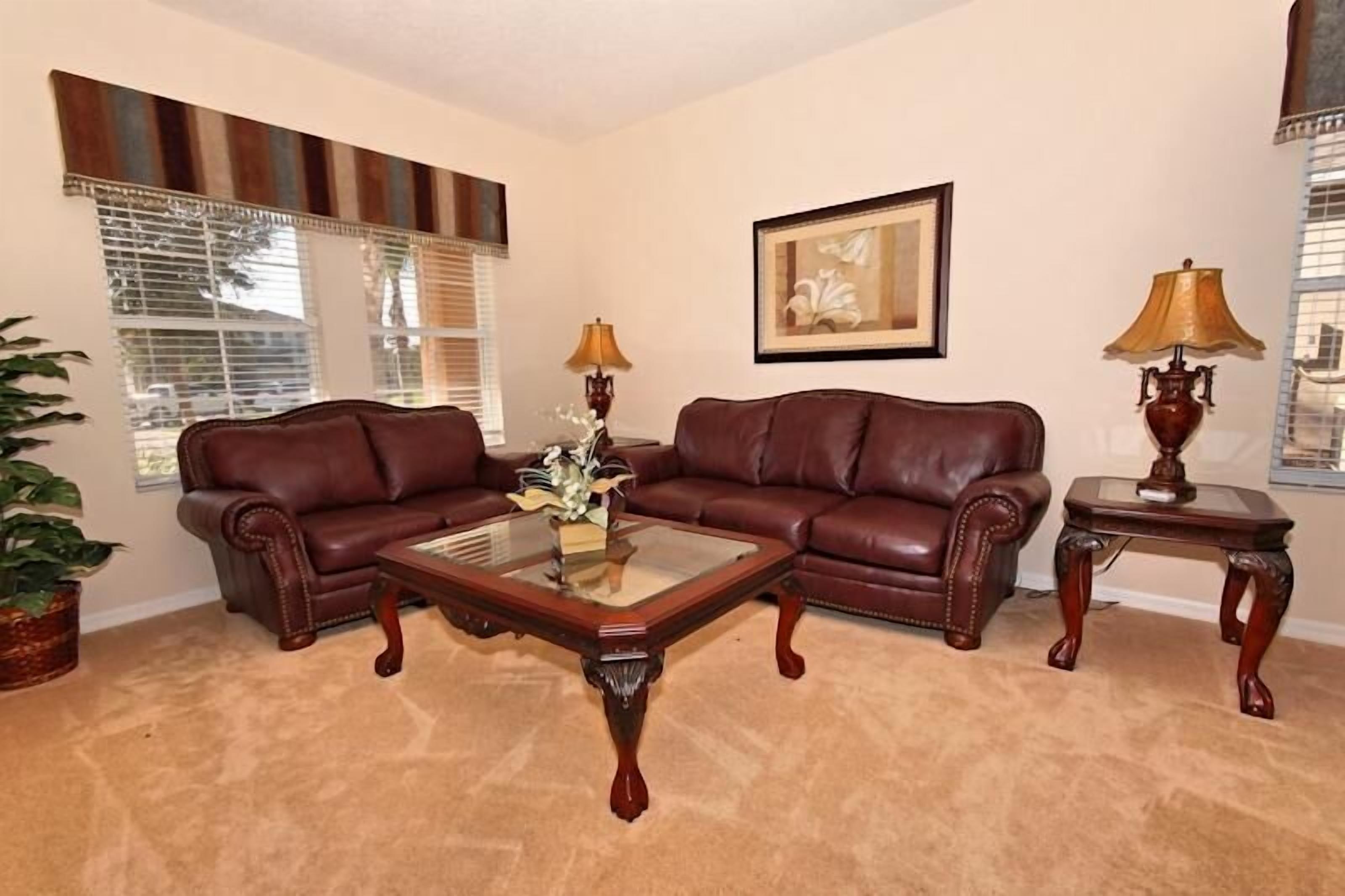 A living room with two brown leather sofas, a glass coffee table, and two wooden side tables with lamps.