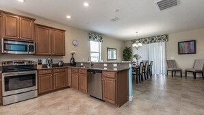 Una cocina moderna con armarios de madera, electrodomésticos de acero inoxidable, una isla central y un comedor con sillas y una mesa.