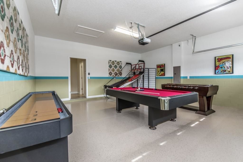 A billiards room with a pool table, a foosball table, and a foosball table in the background.