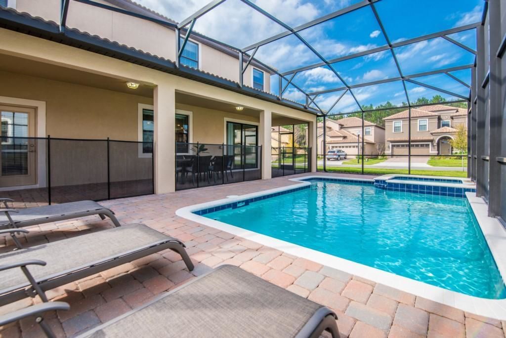 A swimming pool with lounge chairs, a covered patio area, and a view of neighboring houses.