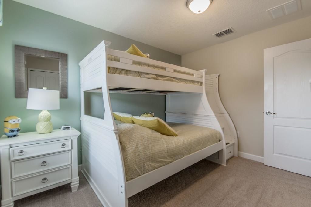A bunk bed with a white frame, a bedside table with drawers, a lamp, and a Minion figurine.