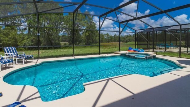 A swimming pool with a clear blue water, surrounded by a covered area with chairs and a hot tub. - Amazing 6 Bedrooms 4 Baths 1028ocb (Bartow)
