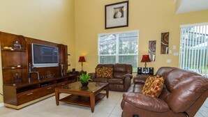 A living room with a wooden entertainment unit, leather sofas, a coffee table, and a TV. - Amazing 6 Bedrooms 4 Baths 1028ocb (Bartow)