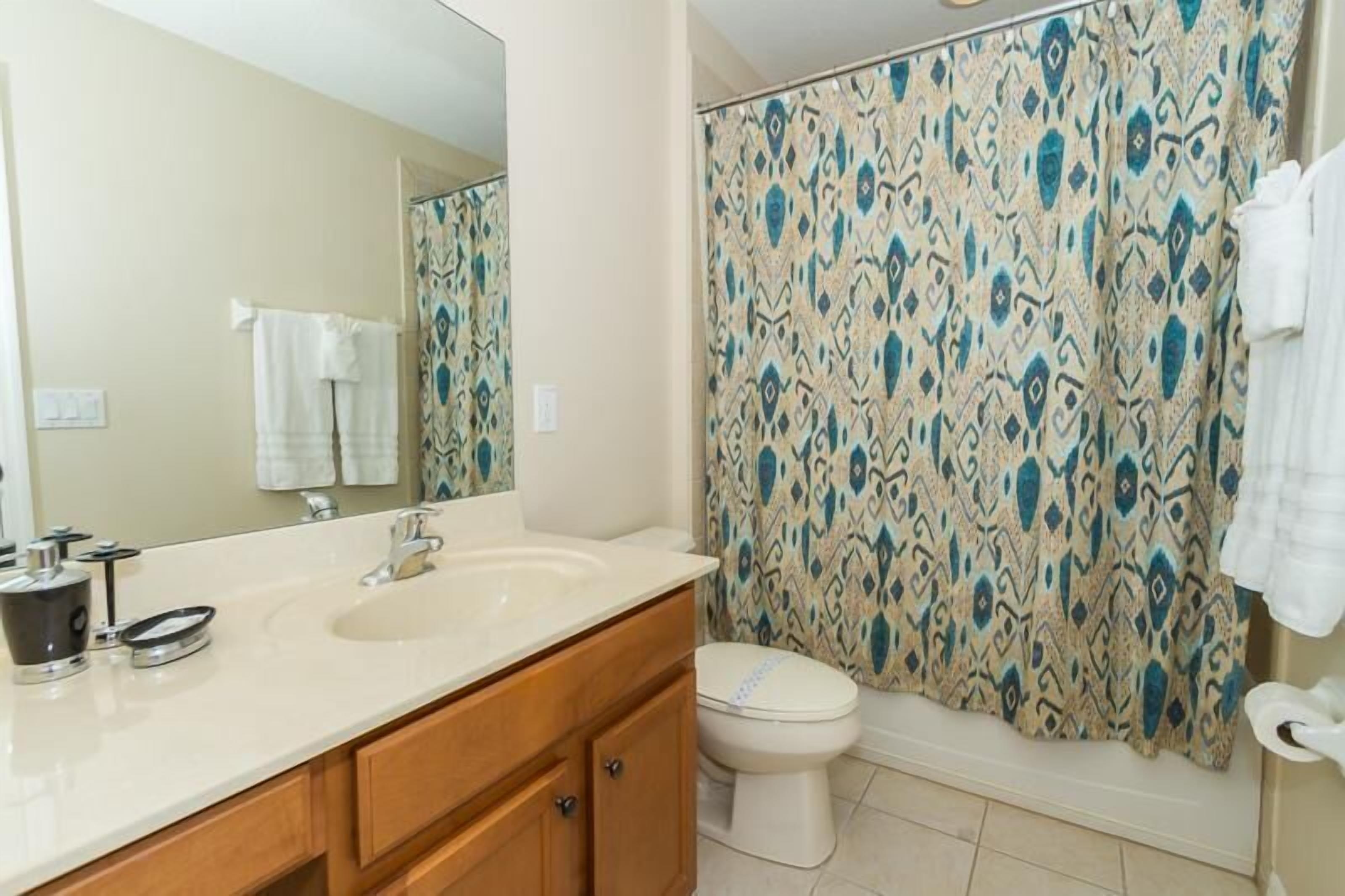 A bathroom with a double sink vanity, a toilet, and a shower with patterned curtains.