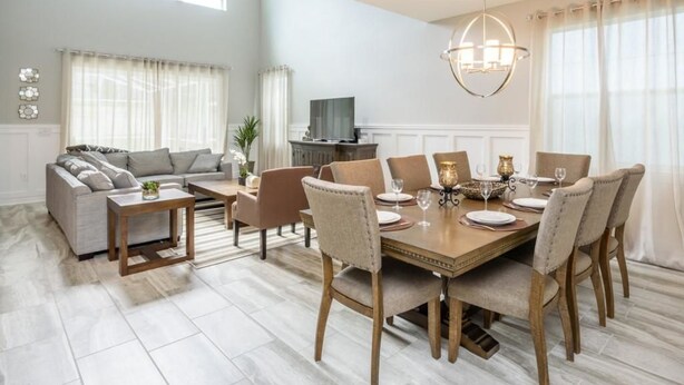 A spacious living room with a large dining table, comfortable seating, and a television in the background. - Amazing NEW 5 Bedrooms Champions Gate! (Davenport)