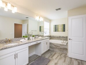Une salle de bain moderne avec un comptoir en granit, des meubles blancs, un grand miroir, une baignoire et une porte.