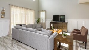 A modern living room with a grey sectional sofa, a wooden coffee table, and a television on a wooden cabinet. - Amazing NEW 5 Bedrooms Champions Gate! (Davenport)