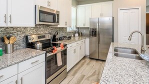 A modern kitchen with white cabinets, stainless steel appliances, granite countertops, and a built-in microwave. - Amazing NEW 5 Bedrooms Champions Gate! (Davenport)