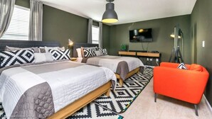 Un dormitorio con dos camas, televisión, escritorio y una silla anaranjada brillante.