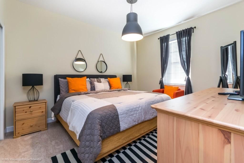 Quarto com cama, mesas de cabeceira, escrivaninha e uma janela grande com cortinas.