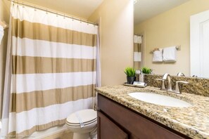 Un baño con cortina de ducha a rayas, un lavabo con encimera de granito, un espejo y un inodoro.