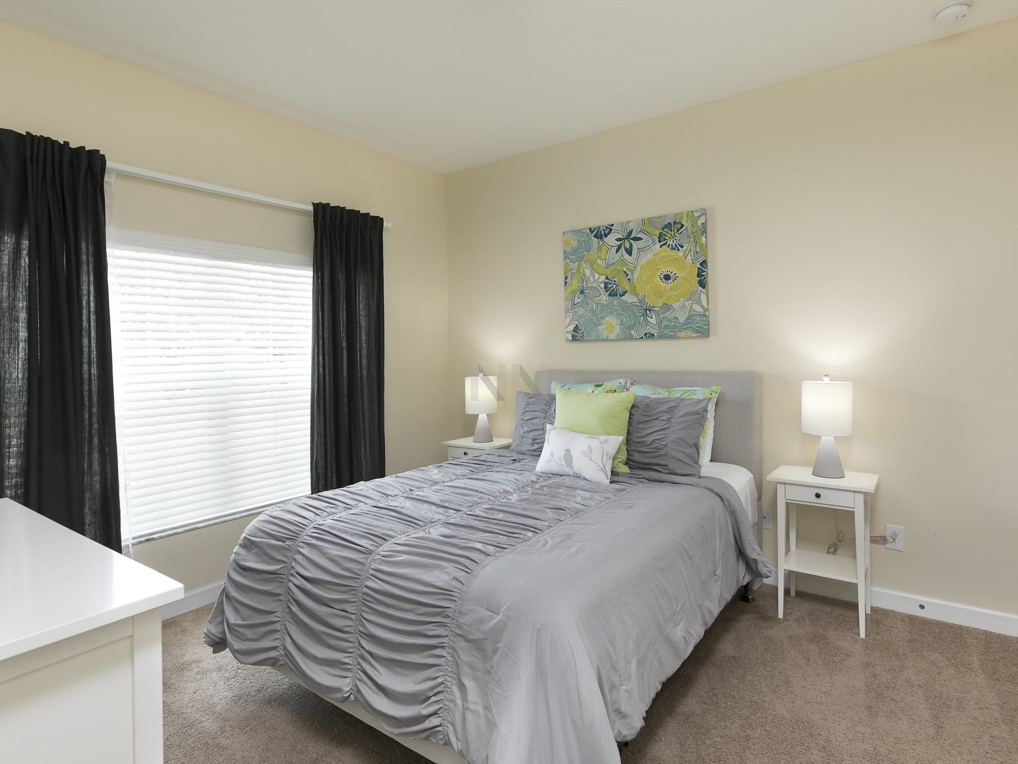 A bedroom with a bed, two bedside tables, a window with curtains, and a wall-mounted painting.