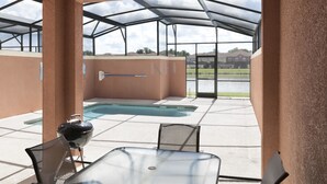 Une terrasse extérieure avec une table et des chaises en verre, un barbecue et une vue sur une piscine et un lac.