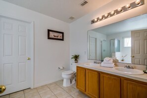 A bathroom with a white toilet, wooden vanity, and a large mirror with lights. - 113bll Disney 5 Bedroom Pool Home With Games Room (Bartow)
