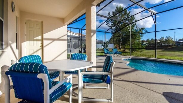 A covered outdoor area with a pool, seating, and a door. - 113bll Disney 5 Bedroom Pool Home With Games Room (Bartow)