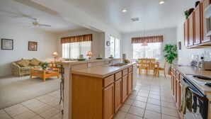 A spacious living area with a large island, a dining table, and a kitchen with wooden cabinets and a stove. - 113bll Disney 5 Bedroom Pool Home With Games Room (Bartow)