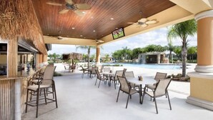 An outdoor patio with tables and chairs, a pool, and a thatched roof structure. - Paradise Palms 6 Bedrooms 5 Baths Best (Kissimmee)