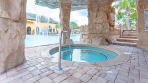 A pool area with a hot tub, surrounded by stone walls and a waterfall feature. - Paradise Palms 6 Bedrooms 5 Baths Best (Kissimmee)
