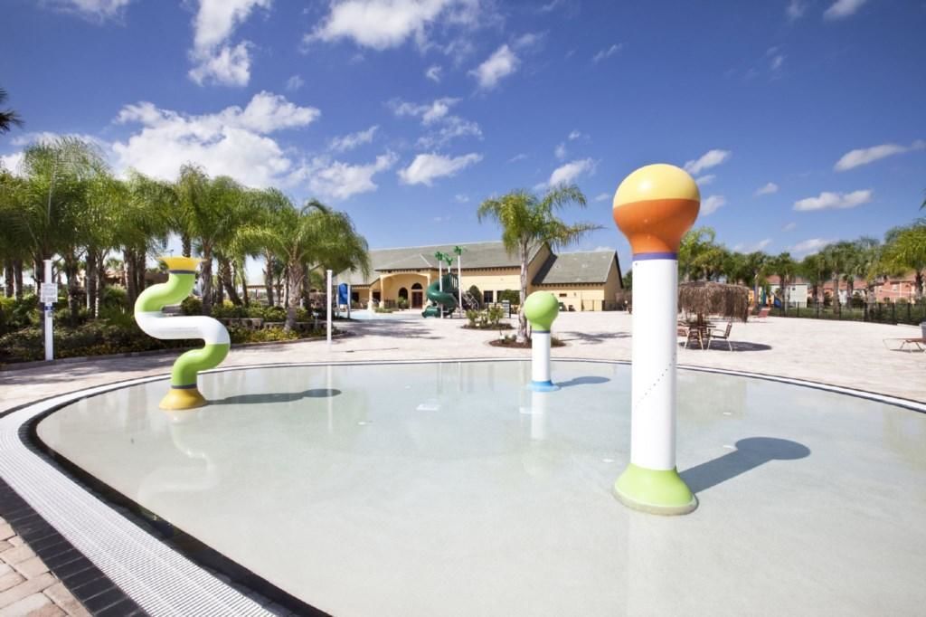A water feature with colorful sculptures in a plaza with palm trees and a building in the background.
