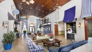 A spacious lobby with a high ceiling, wooden beams, and a central seating area with sofas and a coffee table. There are potted plants and a reception desk with a blue curtain. - Paradise Palms 6 Bedrooms 5 Baths Best (Kissimmee)