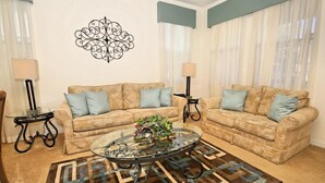 A living room with two beige sofas, a glass coffee table, and a patterned rug. - 103bll Fantastic 4 bed With Games Room (Bartow)